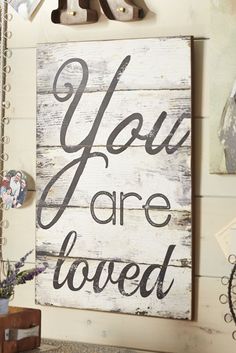 a wooden sign that says you are loved hanging on a wall next to a vase with flowers