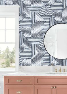 a bathroom with blue and white wallpaper, pink cabinets and a large round mirror