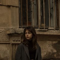 a woman standing in front of an old building with bars on the window sill