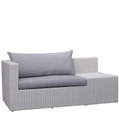 a white wicker couch with grey cushions and pillows on it's back end