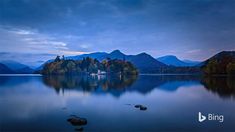 an island in the middle of a lake with mountains in the background at night time