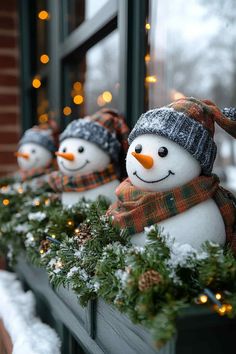 three snowmen sitting on top of a window sill covered in christmas garland and lights