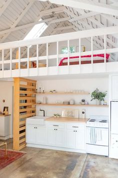 a kitchen with white cabinets and wooden shelves under a lofted bed over a stove top oven