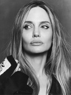 a black and white photo of a woman with long blonde hair wearing a jacket looking at the camera