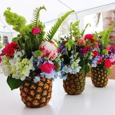 three pineapple shaped vases filled with flowers and greenery on a white table