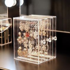 a clear box filled with lots of different types of jewelry on top of a wooden table