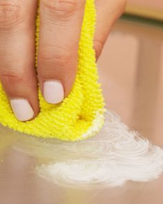 a woman's hand holding a yellow sponge on top of a table