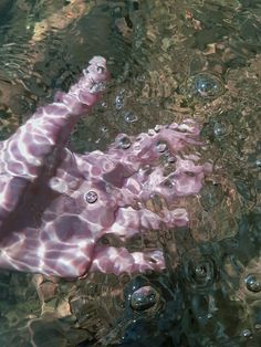 a pink object floating in the water with bubbles on it's back legs and arms