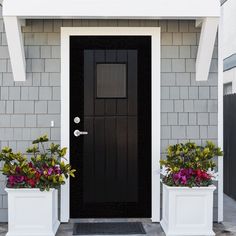 two white planters with flowers in front of a black and gray door on a house