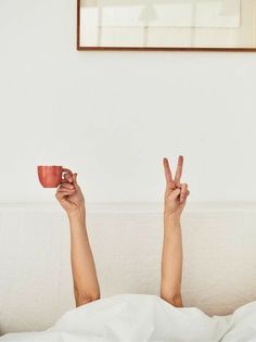 a woman laying in bed with her legs up holding a coffee cup and peace sign