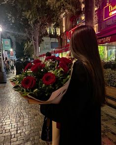 a woman holding a bouquet of red roses on the side of a street at night