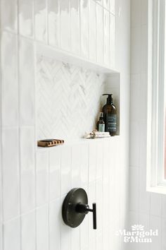 a white tiled bathroom with black fixtures and wood accents on the shower wall, along with hand held soap dispenser