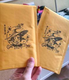 two yellow envelopes with designs on them are held in someone's left hand