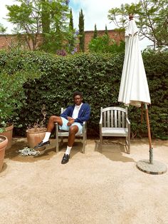 a man sitting in a chair with an umbrella over his head and potted plants behind him