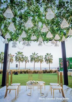 an outdoor wedding setup with white chairs and greenery hanging from the ceiling over it