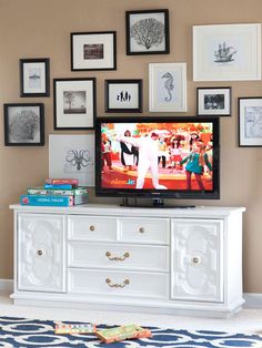 a television is sitting on top of a dresser in front of a wall with pictures