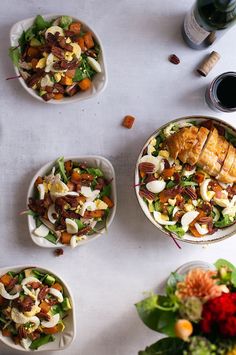 three bowls filled with salad next to two glasses of wine on a white tablecloth