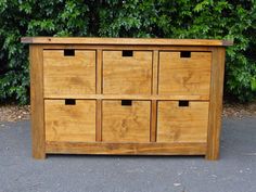 a wooden dresser sitting on top of a sidewalk next to a green bush in the background