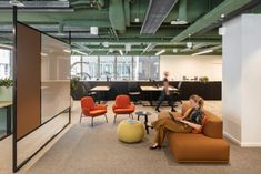 a woman is sitting on a couch in an office with orange chairs and green walls