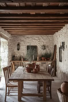 a table and chairs in a room with stone walls, potted plants on either side