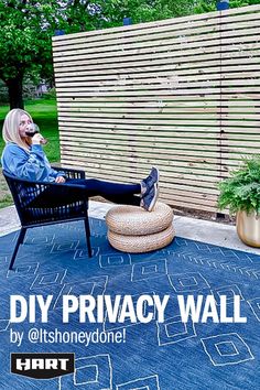 a woman sitting in a chair on top of a blue rug next to a wooden fence