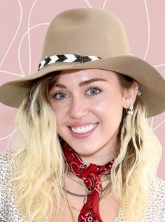 a woman with blonde hair wearing a brown hat and red scarf smiling at the camera