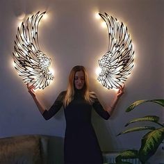 a woman standing in front of a wall with two angel wings on it's arms