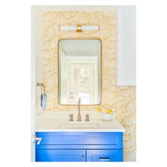 a bathroom vanity with blue drawers and a mirror above it, in front of a yellow wallpapered background