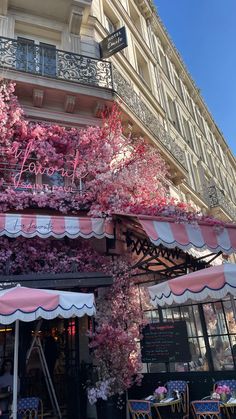 the outside of a restaurant with pink flowers growing on it's walls and awnings