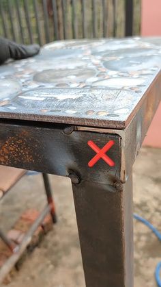 an old metal table with a red x painted on the top and two black chairs behind it