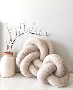 two white pillows stacked on top of each other next to a vase with branches in it