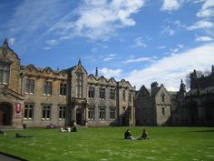 some people are sitting on the grass in front of an old building with many windows