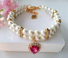 the bracelet is adorned with pearls and a heart shaped pink crystal beaded charm on it