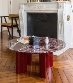 a marble table with red legs in front of a fireplace