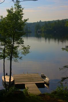 a small boat is docked at the end of a dock on a lake with trees in the foreground