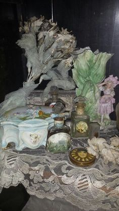 a table topped with lots of different types of vases and figurines on top of a lace covered table cloth