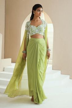 Green long cape with embroidery in pearls, glass beads and white beads. Comes with embroidered choli and draped skirt.
Components:3
Pattern:Embroidered
Type of Work:Floral Motifs
Neckline:Sweetheart
Sleeve Type:Slit Sleeves
Fabric:Skirt and Choli: Georgette, Cape: Organza, Lining: Satin
Color:Green
Other Details:
Floral embroidery
Scalloped hem cape
Draped skirt
Note: The outfit worn by the model on the right is not for sale
Occasion:Mehendi and Haldi - Aza Fashions Lungi Dress Indian For Women, Drape Skirt Outfit Indian, Satin Skirt Outfit Indian, Saree Skirt Drape, Skirt Saree Drape, Long Cape Dress Indian, Drape Skirt Outfit, Bollywood Style Festive Skirt Set With Traditional Drape, Draped Skirt Indian Outfit