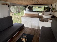 the interior of a camper with wood flooring and white walls, including couches