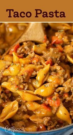 a blue bowl filled with taco pasta next to a wooden spoon on top of a table