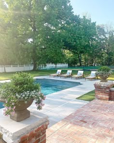 an empty swimming pool surrounded by lawn chairs and flowers in the foreground, next to a brick fire hydrant