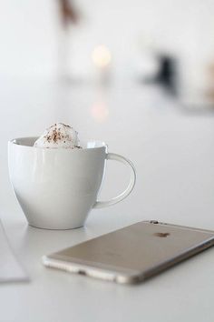 a white coffee cup sitting on top of a table next to an apple laptop computer