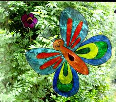 a stained glass butterfly decoration hanging from a window sill in front of some trees