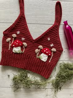 a red knitted bralet with mushrooms and snowflakes on it, next to a purple straw