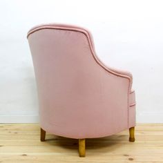 a pink chair sitting on top of a hard wood floor next to a white wall