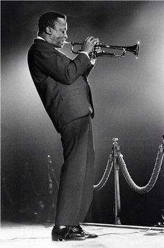 a black and white photo of a man in a suit playing a trumpet on stage