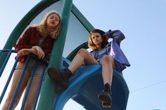 two young women sitting on top of a blue slide