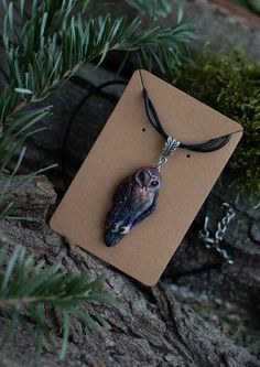 a necklace with an owl on it is sitting on a tree branch in the woods