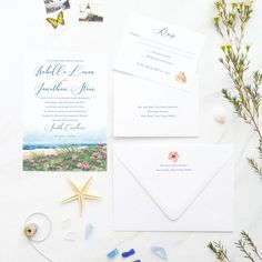 the wedding stationery is laid out on a table with flowers and seashells