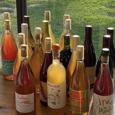 bottles of wine are lined up on a table near a window with grass in the background