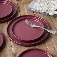 three purple plates with silverware are on a wooden table next to a stack of books